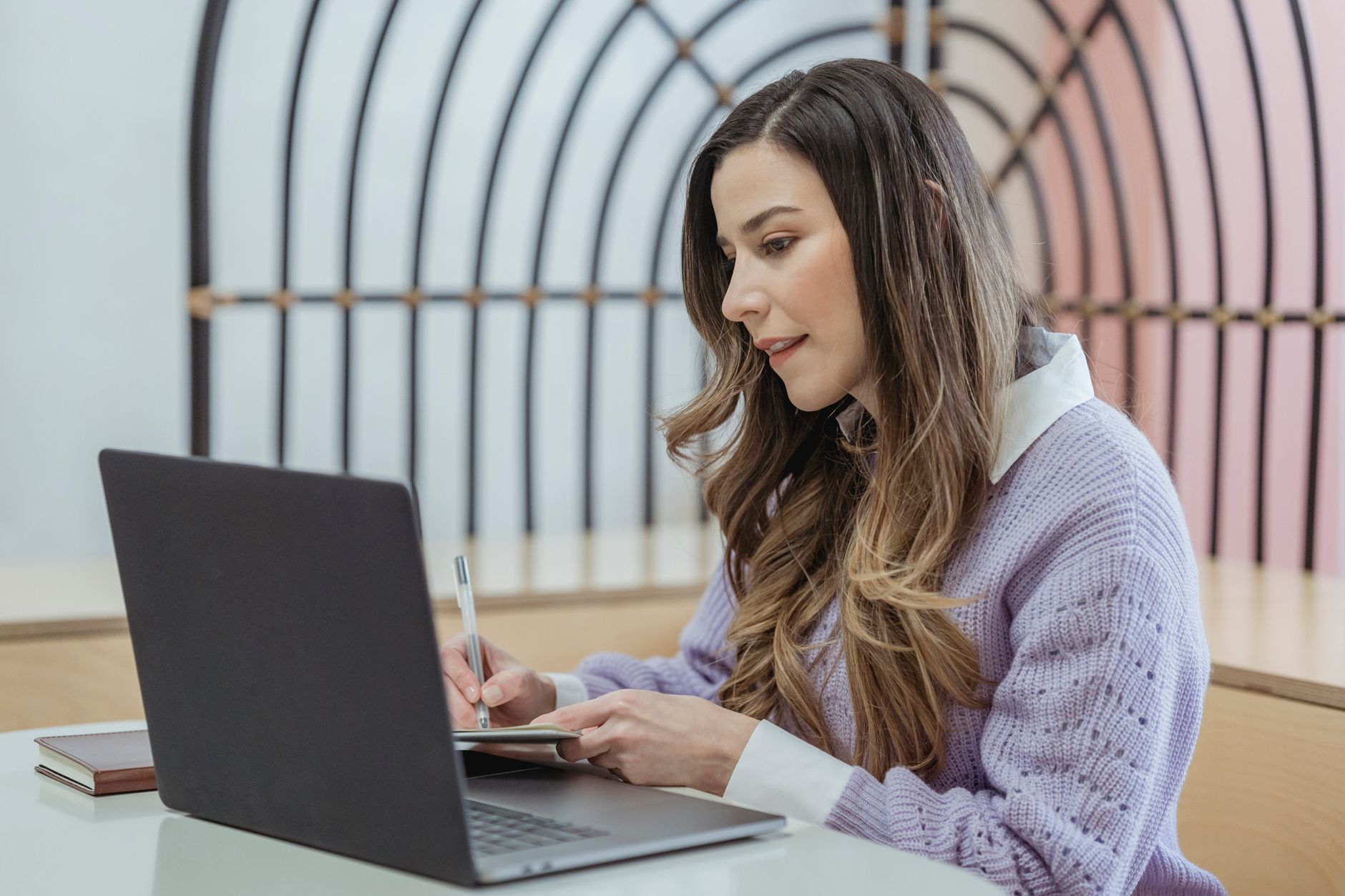 A woman writing notes in a planner beside an open laptop