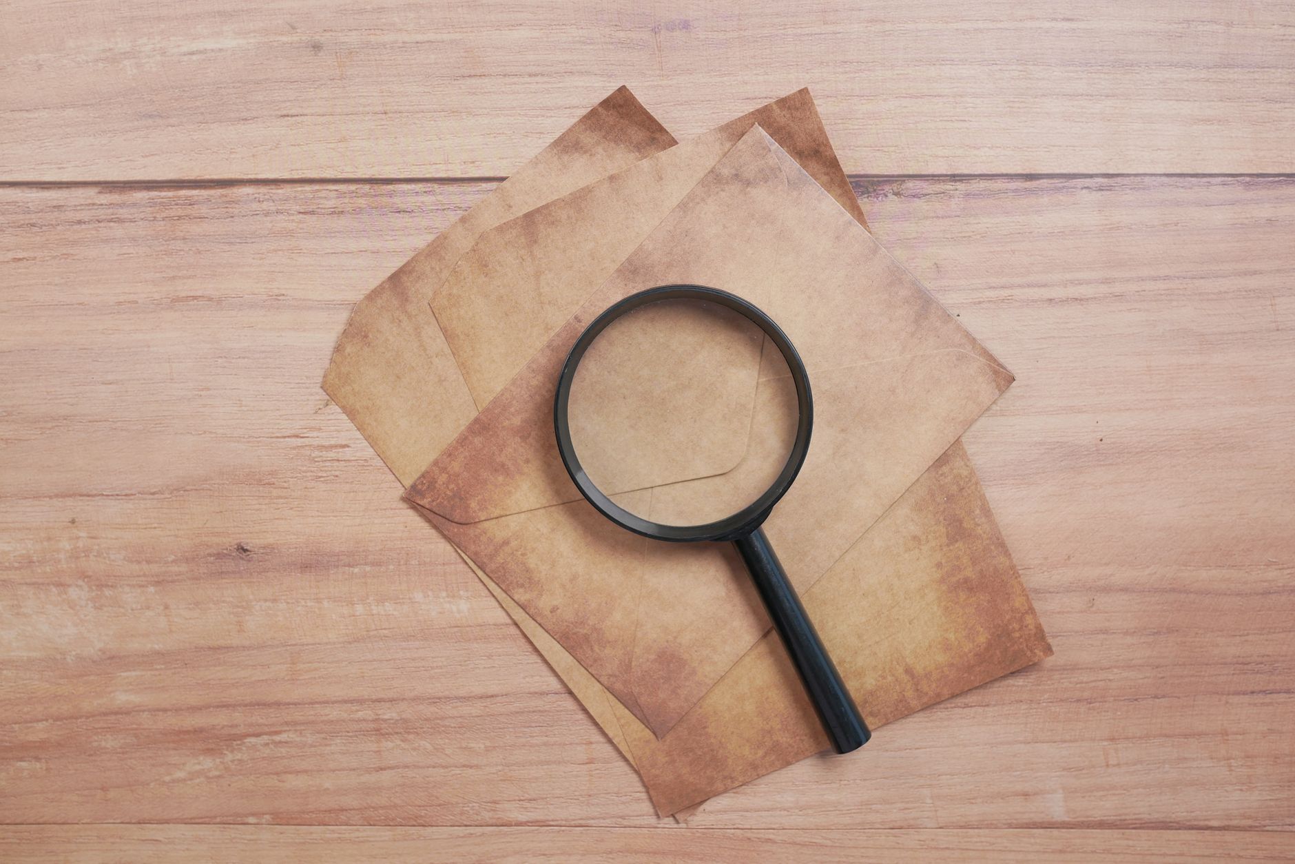 A magnifying glass resting on aged paper on a wooden table