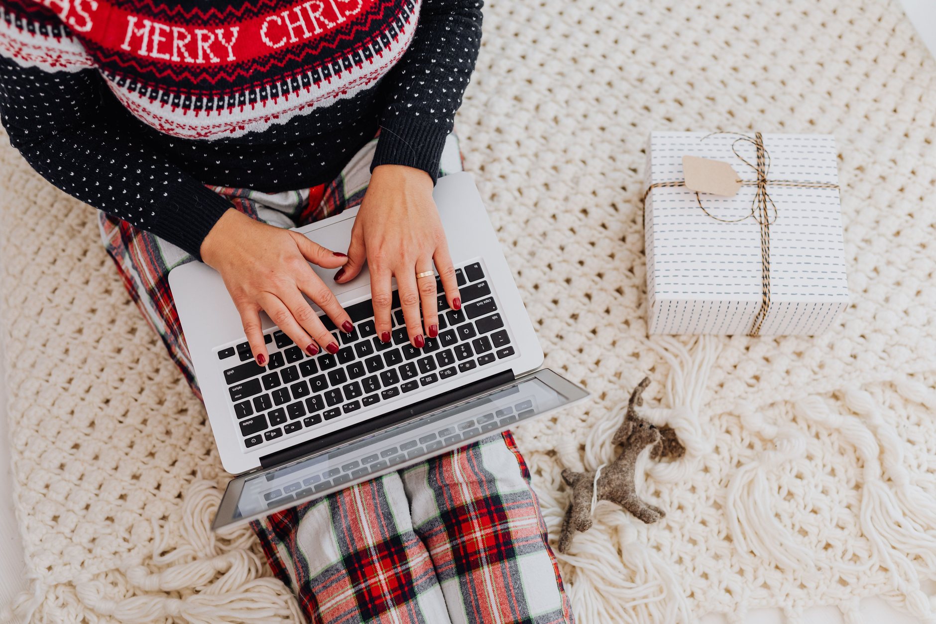 Hands typing on a laptop beside a wrapped holiday gift