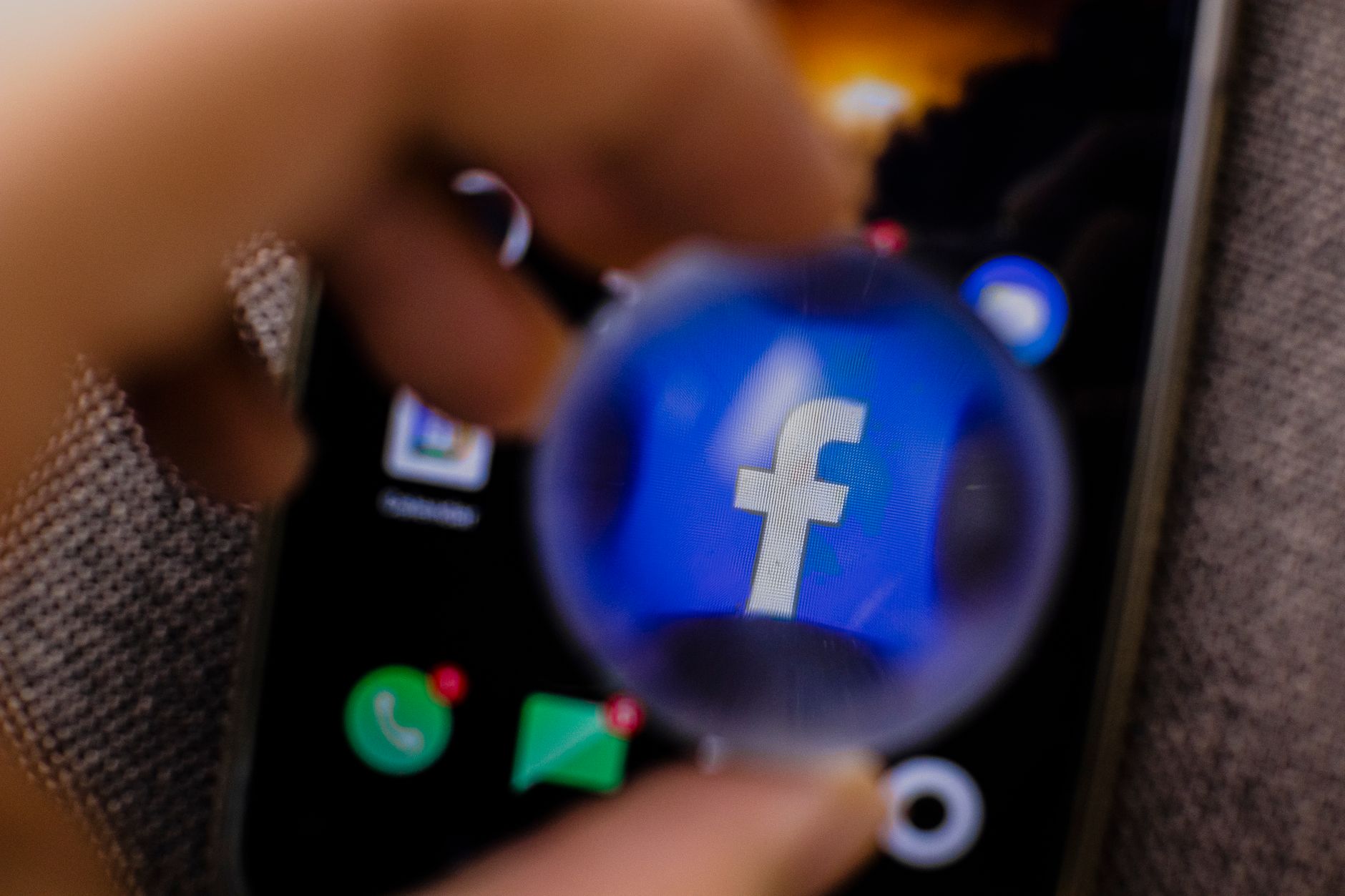 A magnifying glass held over the Facebook app icon on a smartphone screen