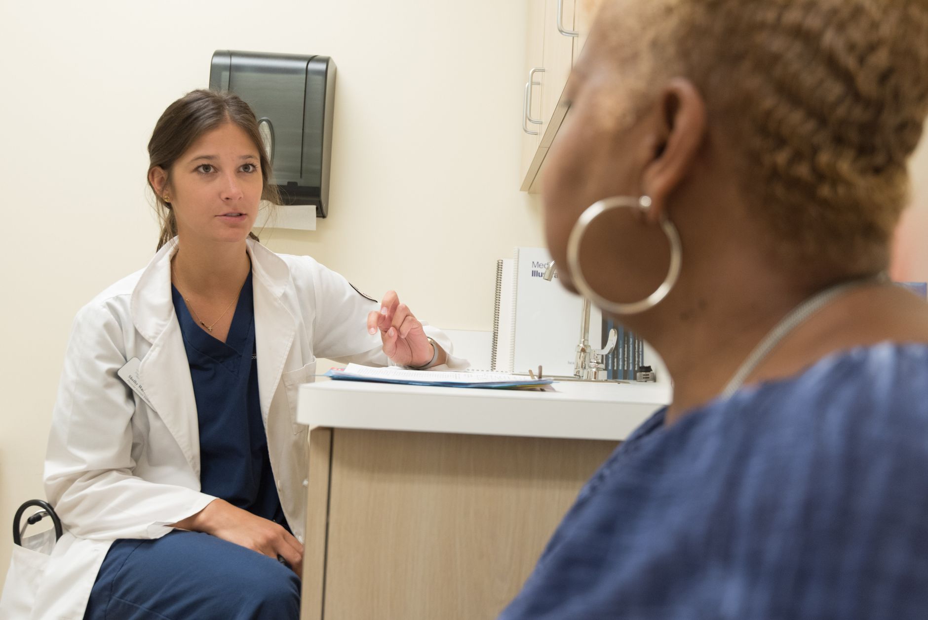 A clinician in a white coat talking with a patient during a consultation