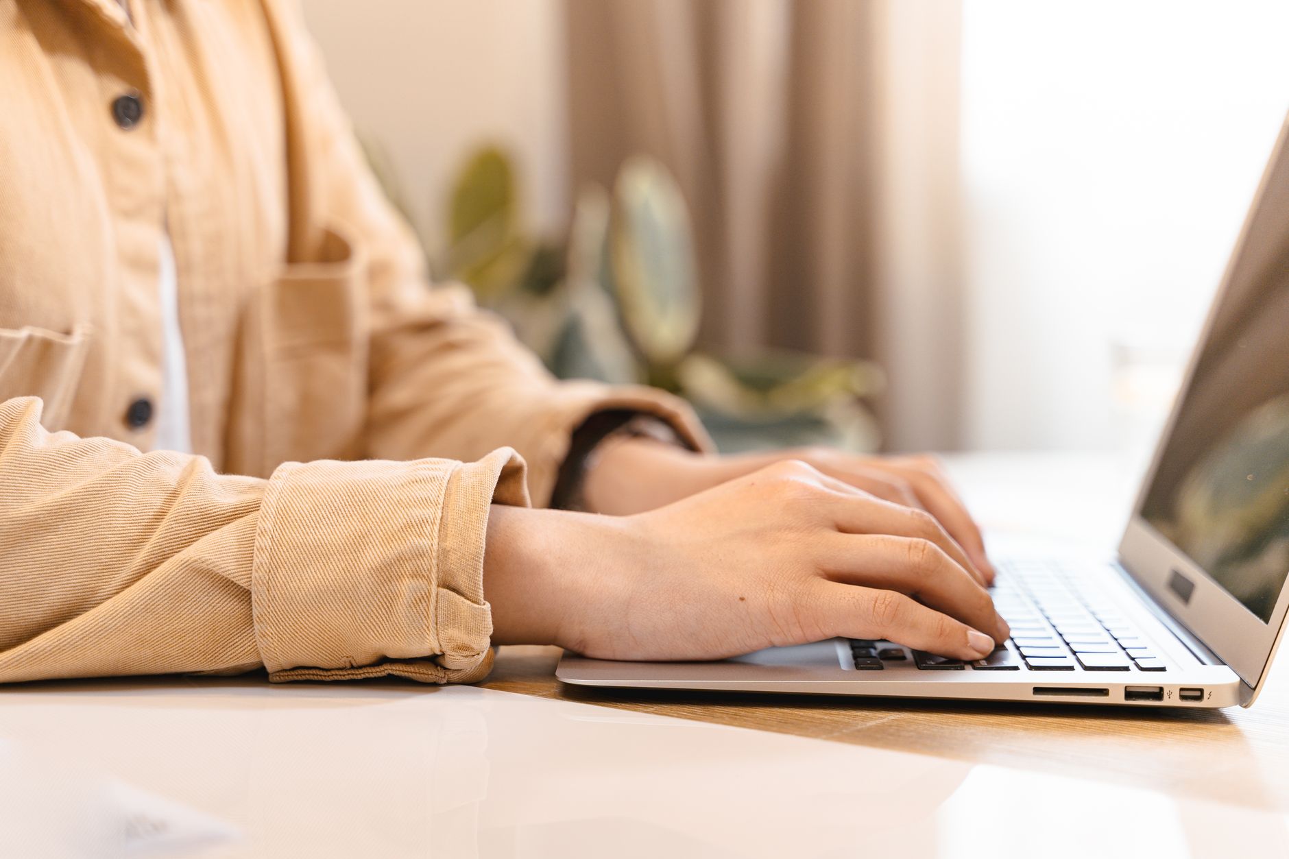 A person typing an email on a laptop at a bright desk